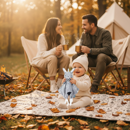 Bébé joue avec son doudou sur un tapis de sol au camping en automne.  Papa et maman discute dans des chaise de camping avec une tasse de café chaud dans les mains