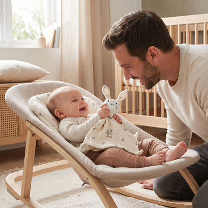 Papa sourit et bebe rigole dans son transat jouant avec son doudou