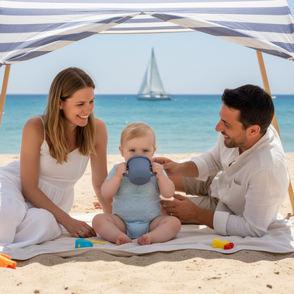 La famille réunie sous la tente de plage à la mer voilier vogue sur l'eau et bébé boit dans sa tasse